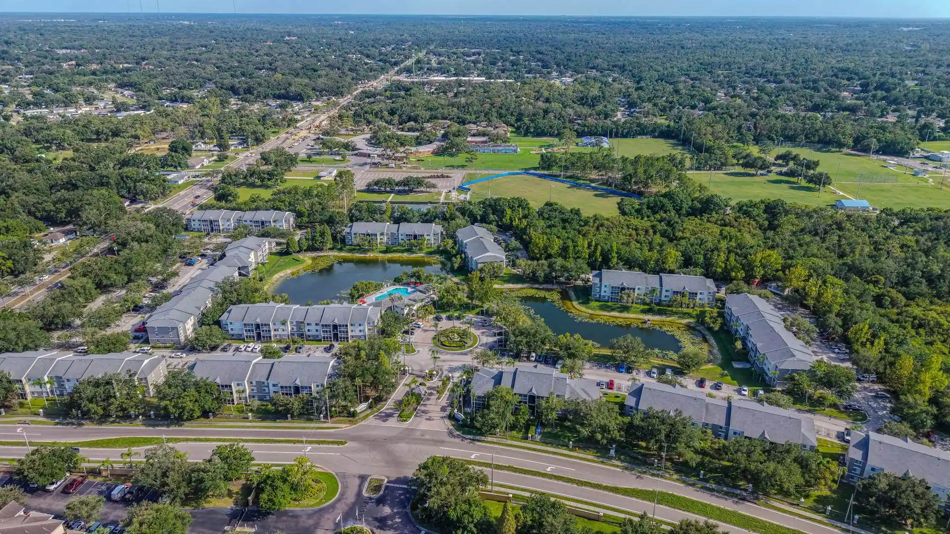 Aerial view of a residential community with apartment buildings, two ponds, lawns and mature oak trees