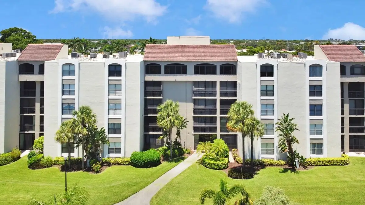 White condominium building behind a green lawn with palm trees