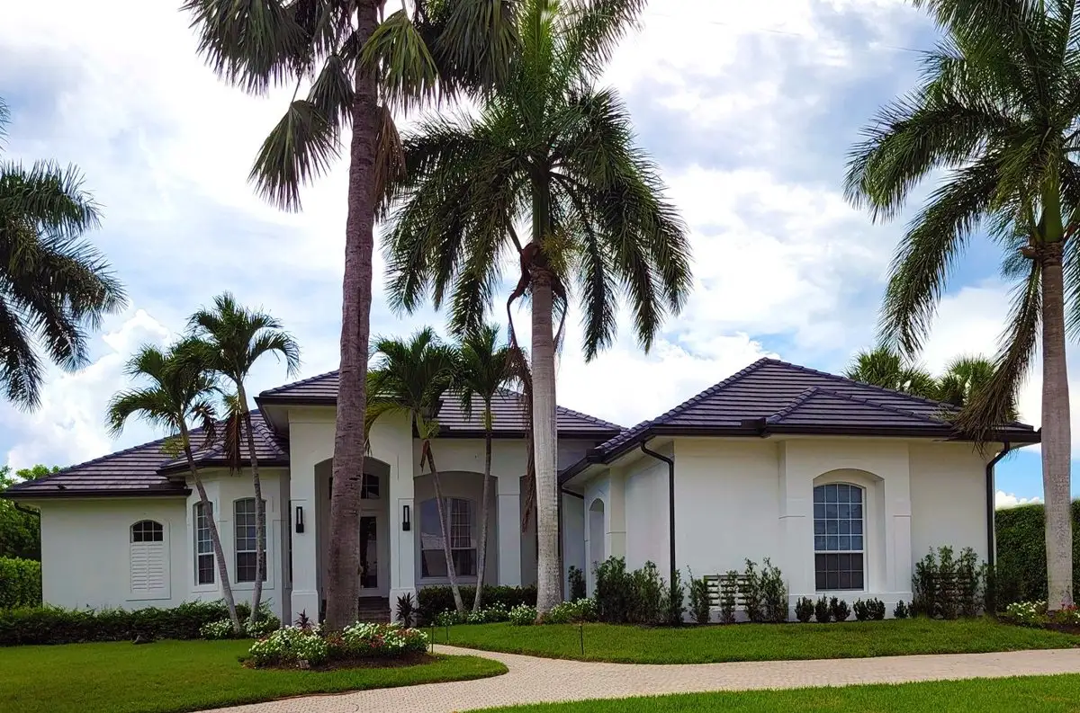 White stucco house with a dark tile roof, tall royal palms and a curved path across the front lawn